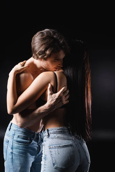 Man in jeans touching brunette girlfriend in bra on black background — Fotografia de Stock