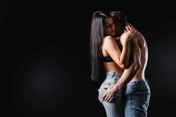 Uomo senza maglietta toccando glutei di fidanzata in jeans isolati su nero — Foto stock