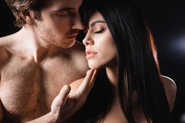Homme torse nu touchant menton de petite amie brune sur fond noir — Photo de stock