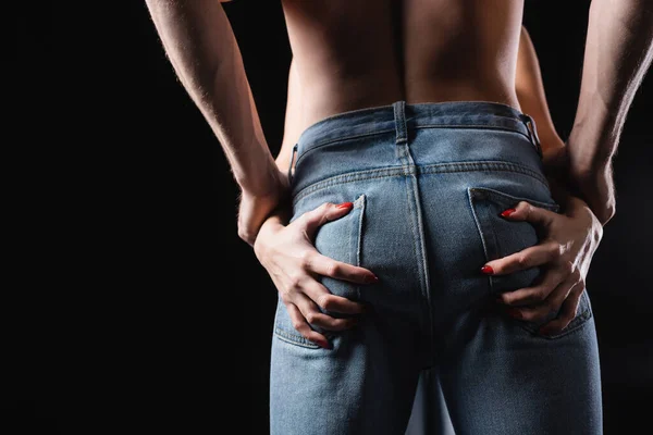Cropped view of passionate woman touching buttocks of boyfriend in jeans isolated on black — Stockfoto