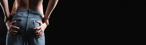 Обрізаний вид жінки, що торкається сідниць хлопця в джинсах ізольовано на чорному, банер — стокове фото