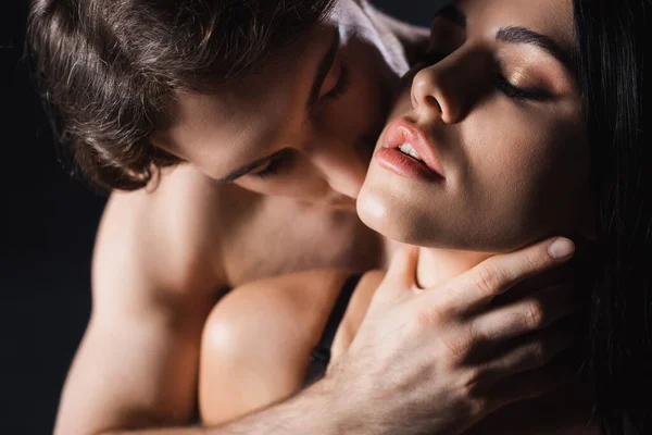 Сексуальна людина торкається шиї дівчини брюнетки з закритими очима ізольовані на чорному — стокове фото