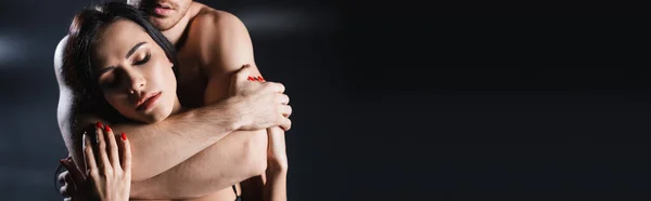 Seductive woman touching hands of muscular man on black background, banner — Stock Photo