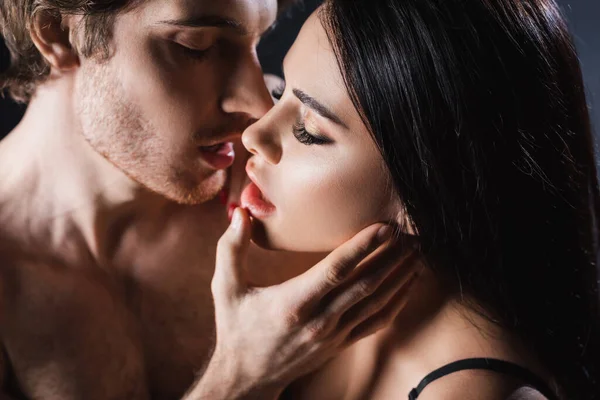 Sexy Mann küsst und berührt Gesicht der brünetten Freundin auf schwarzem Hintergrund — Stockfoto