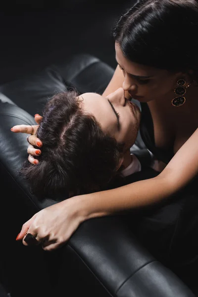 Visão aérea de mulher apaixonada beijando namorado no sofá de couro isolado no preto — Fotografia de Stock