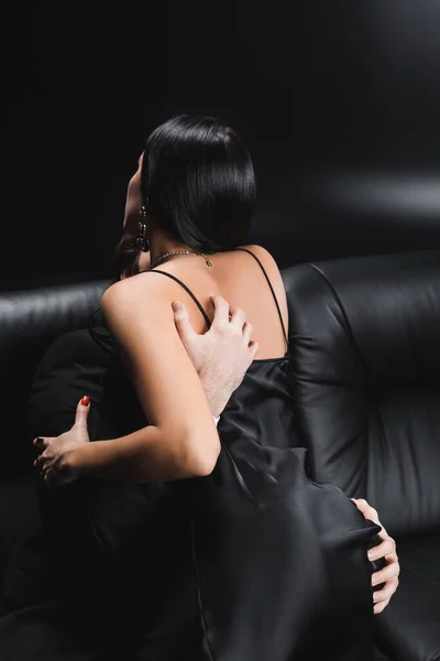 Чоловік торкається сідниць пристрасної жінки в шовковій сукні на дивані на чорному тлі — стокове фото