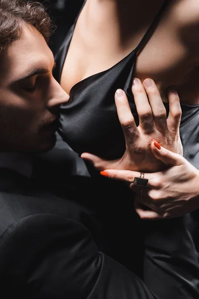 Man in suit touching breast of sexy girlfriend in satin dress on black background — Stock Photo