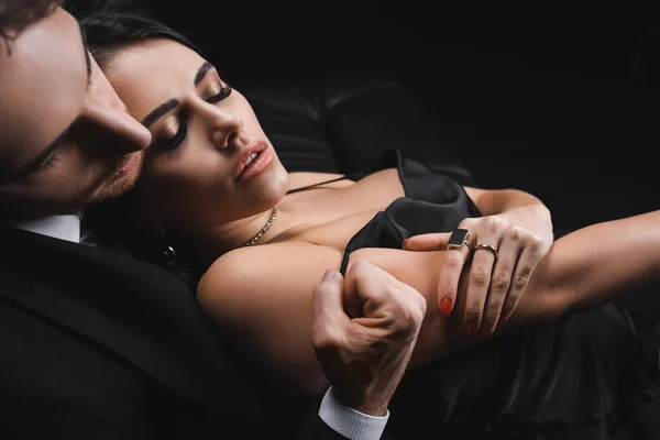 Man in suit undressing sensual woman in silk dress isolated on black - foto de stock
