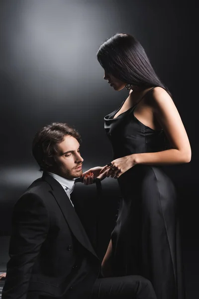 Mulher sexy puxando gravata no namorado no desgaste formal no fundo preto — Fotografia de Stock