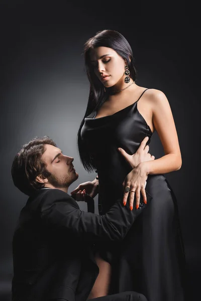 Hombre en ropa formal tocando novia sexy en vestido de satén sobre fondo negro - foto de stock