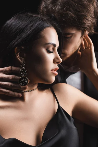Young man in formal wear kissing sexy brunette girlfriend isolated on black — Fotografia de Stock