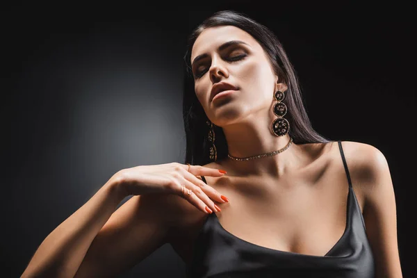 Sexy brunette woman in silk dress touching chest on black background — стоковое фото