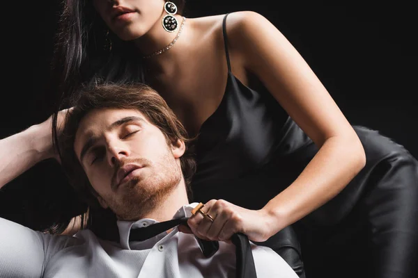 Sexy Frau zieht Freund in Hemd und Krawatte auf Couch isoliert auf schwarz aus — Stockfoto
