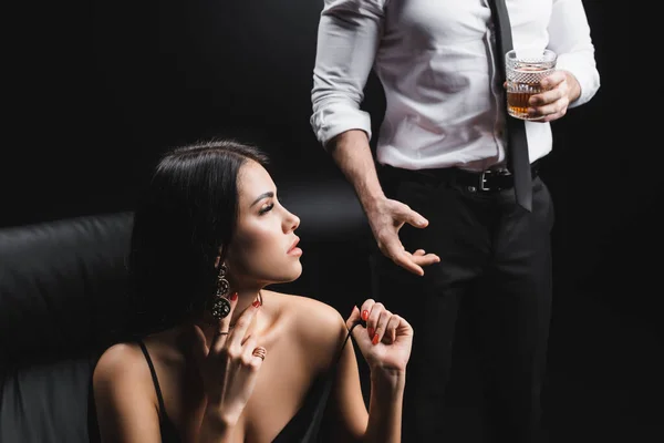 Sexy woman taking off dress near boyfriend in formal wear with glass of whisky isolated on black — Fotografia de Stock