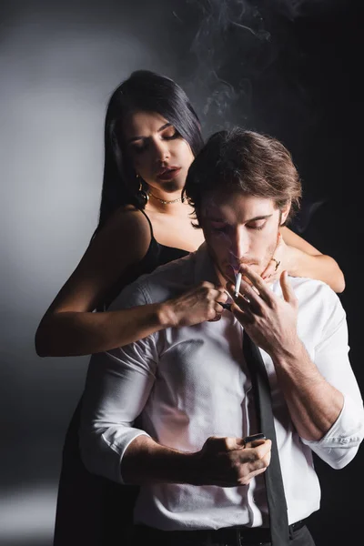 Sensual woman touching boyfriend smoking cigarette on black background — Stock Photo