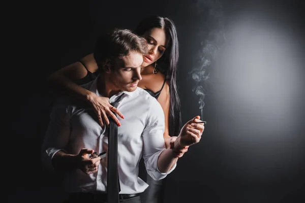 Sexy woman touching boyfriend with lighter and cigarette on black background — Stockfoto