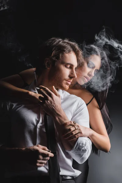 Brunette woman touching boyfriend in formal wear with cigarette on black background — Fotografia de Stock