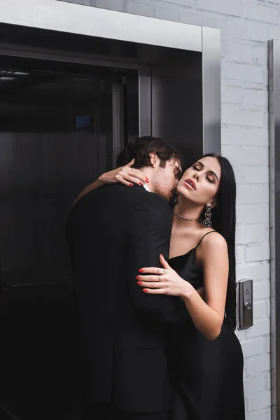 Man in formal wear kissing sexy girlfriend near elevator — Stock Photo