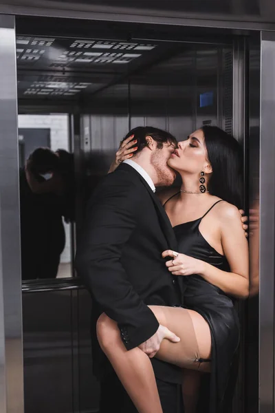 Passionate man kissing sexy girlfriend in satin dress near elevator — Photo de stock