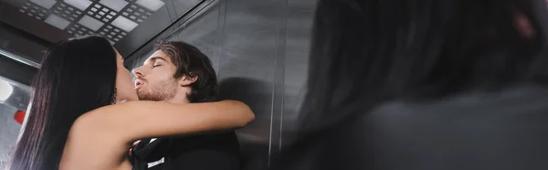 Низкий угол зрения брюнетка женщина целует элегантный парень в лифте, баннер — стоковое фото