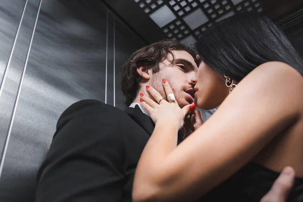 Vista basso angolo di donna sexy baciare elegante fidanzato in tuta in ascensore — Foto stock