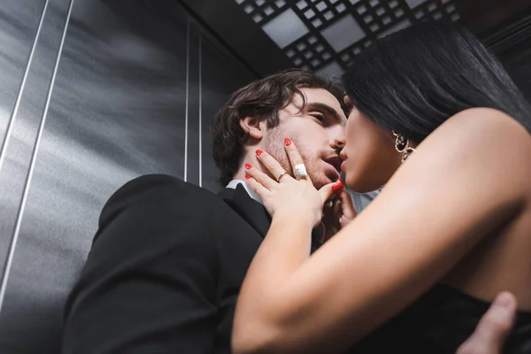 Baixo ângulo vista de mulher sexy beijando namorado elegante em terno no elevador — Fotografia de Stock