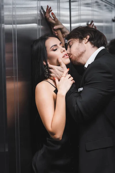 Elegant man kissing sexy girlfriend in silk dress in elevator — Photo de stock
