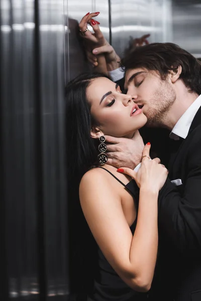 Sexy man kissing and touching neck of seductive girlfriend in elevator — Stock Photo