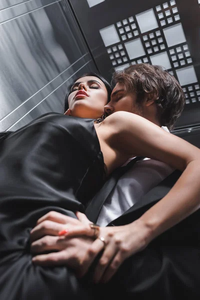 Visão inferior do homem apaixonado tocando e beijando namorada em vestido de seda no elevador — Fotografia de Stock