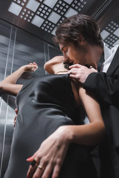 Low angle view of sexy man kissing girlfriend in silk dress in elevator — Stock Photo