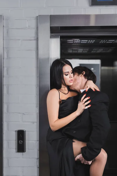 Morena homem de terno beijando mulher sexy no vestido perto do elevador — Fotografia de Stock