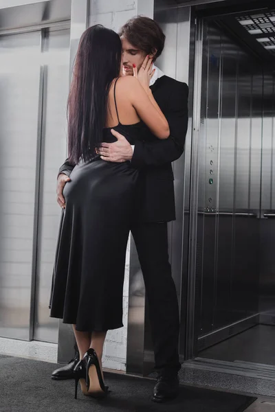 Femme sexy en robe et talons embrasser petit ami près de l'ascenseur dans le hall — Photo de stock