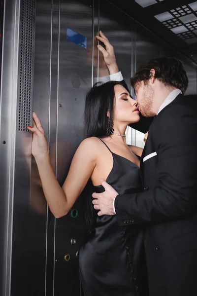 Mulher sensual em vestido preto beijando namorado no elevador — Fotografia de Stock