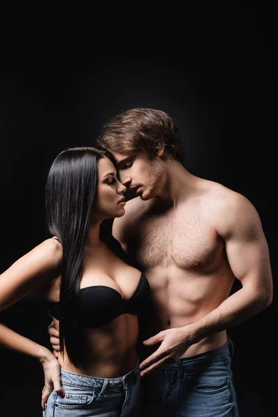 Sexy shirtless man hugging girlfriend in bra isolated on black — стоковое фото