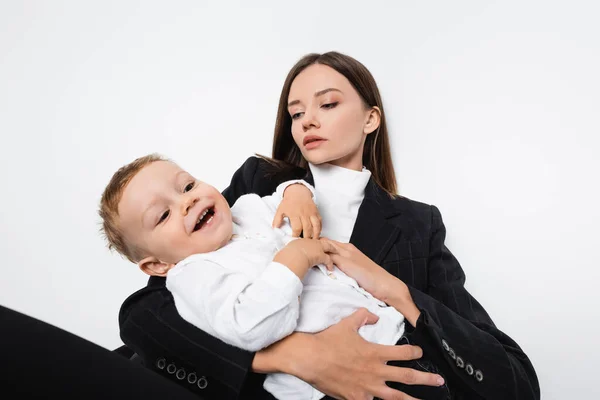 Menino feliz rindo perto da mãe em terno preto isolado no branco — Fotografia de Stock