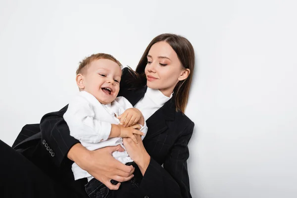 Vista superior da mulher sorridente em terno preto segurando filho alegre no branco — Fotografia de Stock