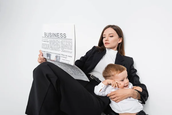 Жінка в чорному костюмі читає бізнес-газету біля щасливого сина на білому — стокове фото