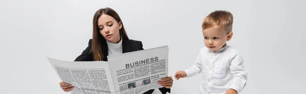 Woman reading business newspaper near little son isolated on grey, banner — стоковое фото