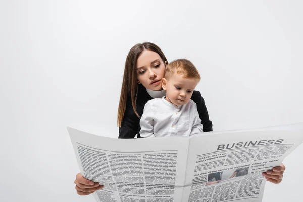 Молода бізнес-леді читає газету біля дитини малюка ізольовані на сірому — стокове фото