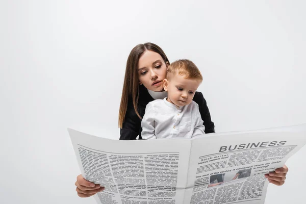 Young businesswoman reading newspaper near toddler child isolated on grey — стоковое фото