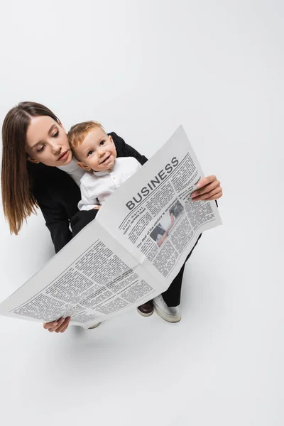Visão de alto ângulo da mulher lendo jornal de negócios perto do filho feliz no branco — Fotografia de Stock
