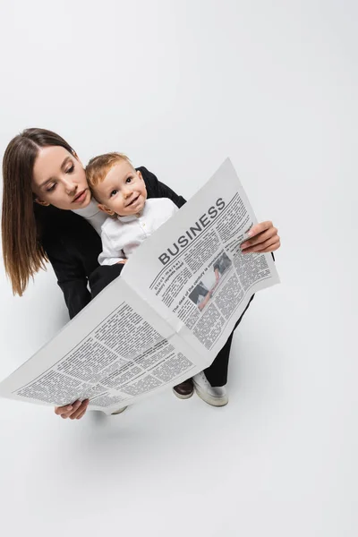 High angle view of woman reading business newspaper near happy son on white — Stock Photo