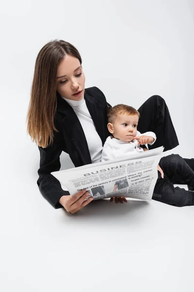 Jovem empresária ler jornal perto de pequeno filho no branco — Fotografia de Stock