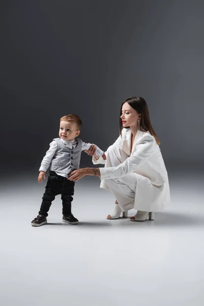 Femme en costume blanc soutenant enfant en bas âge fils debout sur gris — Photo de stock