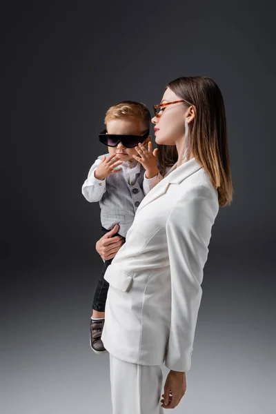 Jeune femme en costume élégant debout avec fils portant des lunettes de soleil sur gris — Photo de stock