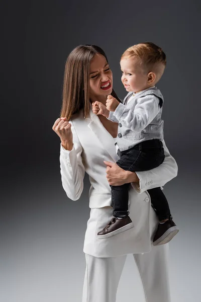 Excited mother and son showing win gesture on grey — Foto stock