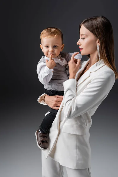 Мати і син в стильному одязі торкаються губ на сірому — стокове фото