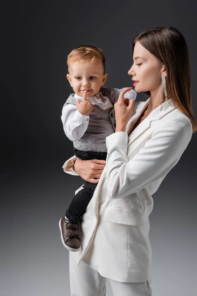 Mother and son in stylish clothes touching lips on grey — Fotografia de Stock