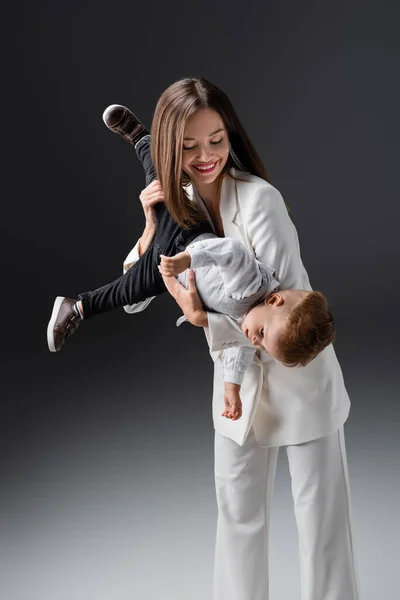 Радісна жінка тримає маленького сина, розважаючись на сірому — стокове фото