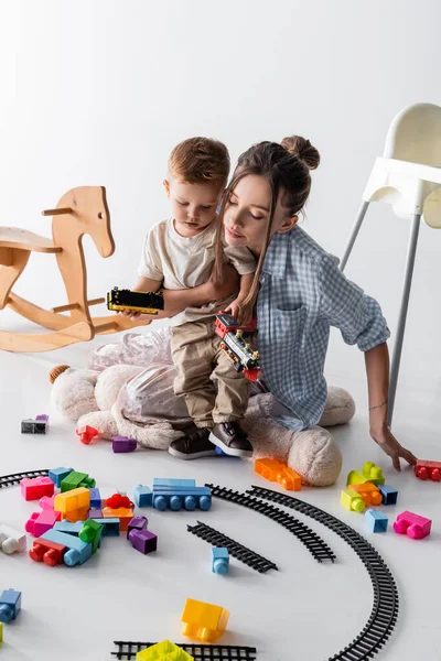 Kleiner Junge mit junger Mutter spielt mit Spielzeugeisenbahn auf weiß — Stockfoto